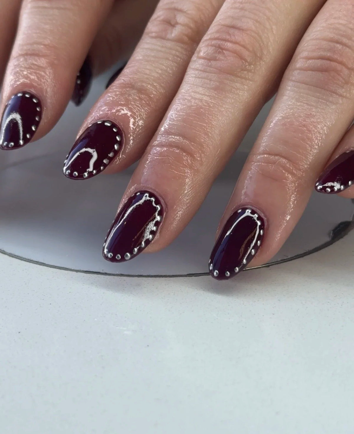 Dark burgundy manicure with a white dotted line detail from Oh Baby Salon and Spa in Bloomington, Illinois