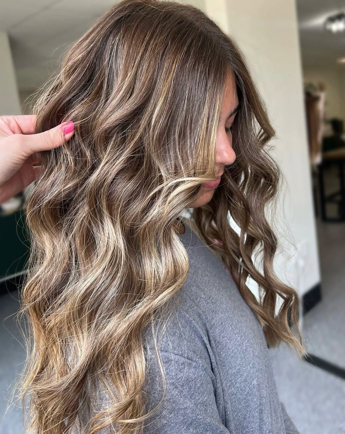 Stylist holding a curled section of long brunette hair with warm highlights at Oh Baby Salon & Spa in Bloomington, Illinois