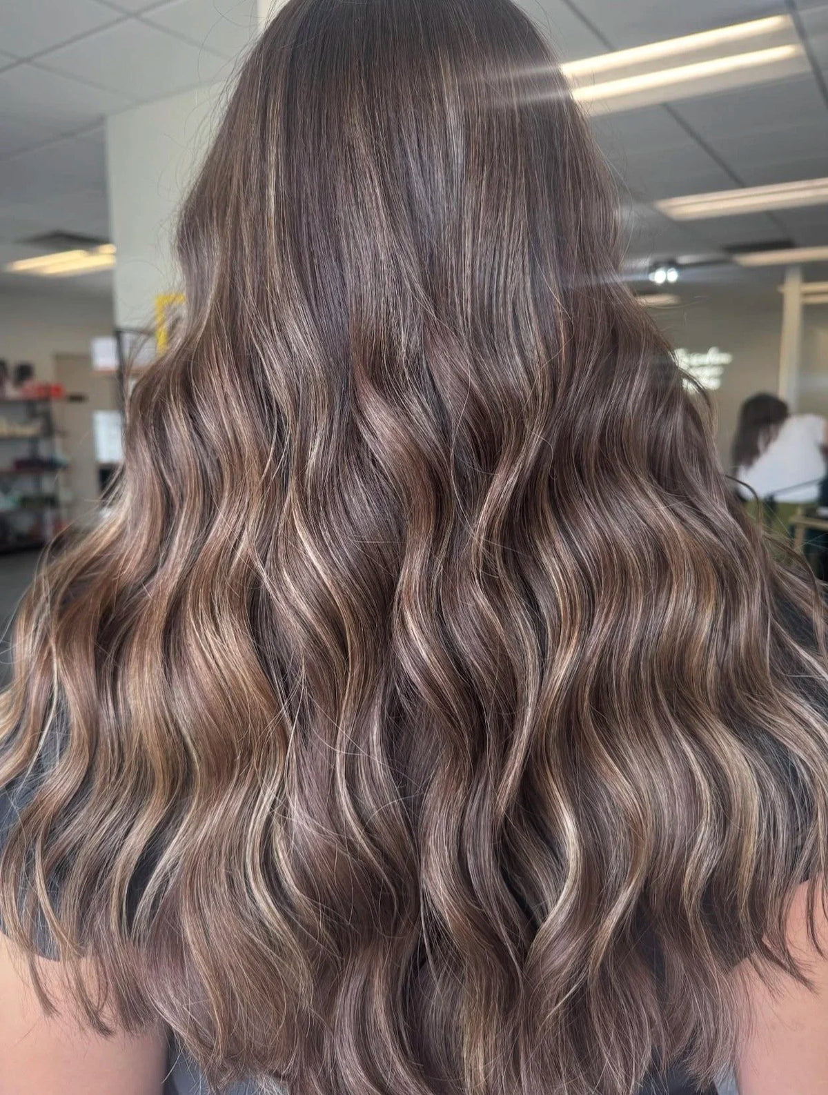 Cool-toned brunette hair with lighter dimension styled in waves at Oh Baby Salon & Spa in Bloomington, Illinois